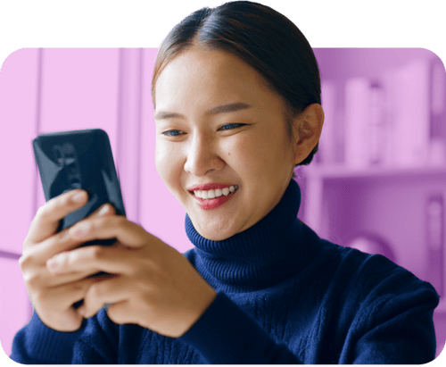 A woman smiles brightly while holding a cell phone in her hand, exuding joy and positivity.